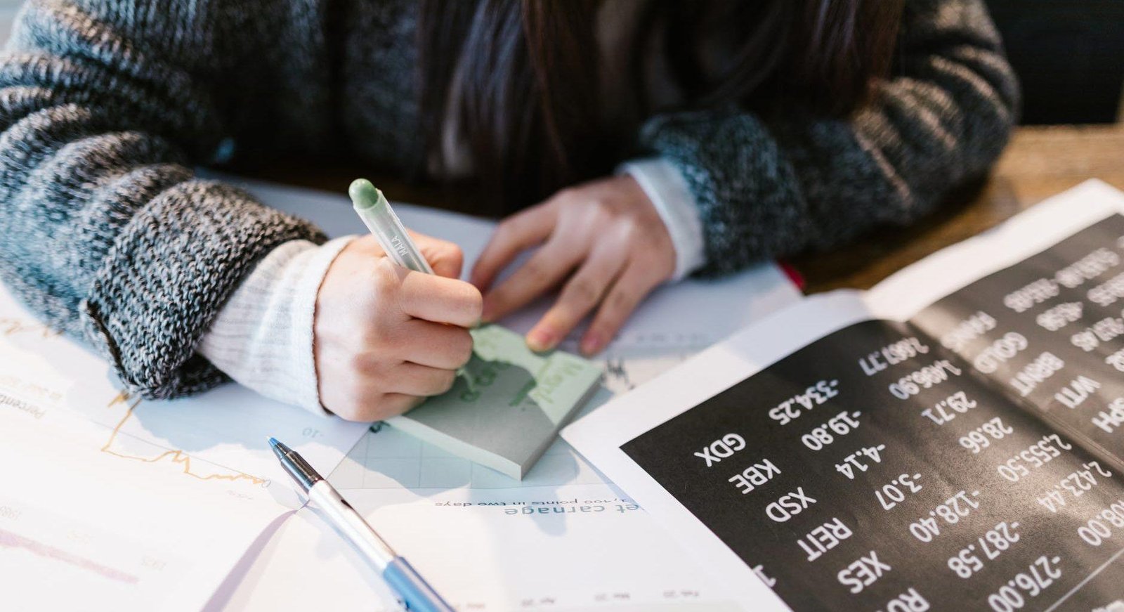 woman in gray sweater holding pen writing on white paper