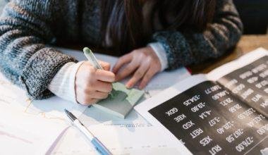 woman in gray sweater holding pen writing on white paper