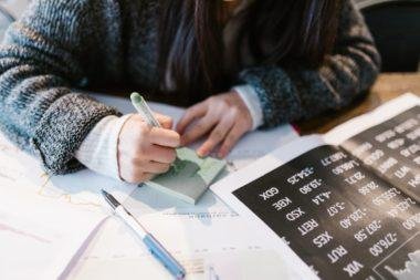 woman in gray sweater holding pen writing on white paper